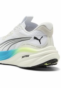 Zapatilla de running blanca con acentos negros, parte superior de malla texturizada y una suela gruesa con un degradado que va de azul a verde claro, con la marca 'NITRO'.