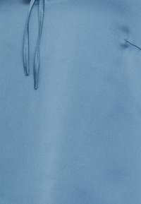 Hoodie azzurro chiaro in tessuto morbido e testurizzato. Include cappucci regolabili e una tasca a marsupio frontale. Design semplice, senza ulteriori motivi.