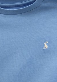 Tissu bleu clair avec un petit lapin blanc brodé près de la poitrine et un col rond.