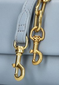 Lichtblauwe leren handtas met goudkleurige hardware, inclusief twee sluitingen en een kettingdetail bevestigd aan een gestikte strap.