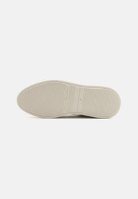 Plochá béžová podrážka s jemnými vodorovnými drážkami, značka "Tommy Hilfiger" a velikost 31 vyražená ve střední části.