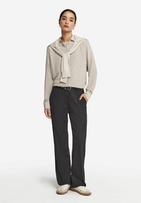 Helles beiges Langarmbluse mit einem über die Schultern gelegten Pullover, kombiniert mit schwarzen, maßgeschneiderten Hosen und weißen Sneakern mit braunen Sohle.