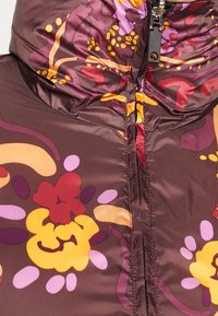 Veste courte matelassée marron avec un motif floral dans des teintes de violet, jaune et rouge, dotée d'un col montant et d'une fermeture éclair. Texture lisse et brillante.