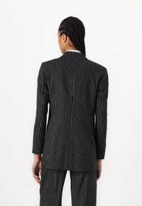 Pinstripe blazer in black with white stripes, tailored fit, single vent at the back, accompanied by matching trousers. Textured fabric.