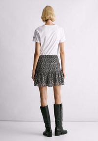 Weißes Kurzarm-T-Shirt, getragen mit einem schwarz-weiß gemusterten Minikleid, das einen ausgestellten Saum hat und mit kniehohen schwarzen Stiefeln kombiniert wird.