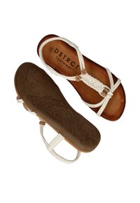 Sandales blanches tressées avec une semelle extérieure texturée marron présentant des motifs de vagues et une marque DSTRCT sur la semelle intérieure.