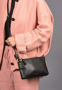 Bolso de cuero negro con forma rectangular, que presenta un cierre en la parte superior, acentos de hardware en dorado y una correa desmontable. La textura parece suave.