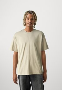 Lichtbeige katoenen t-shirt met korte mouwen en een ronde hals, gecombineerd met donkergrijze denim jeans. Casual pasvorm.