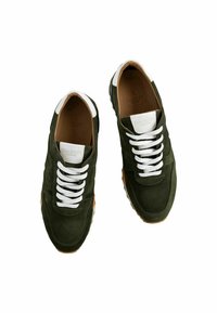 Mörkgröna mockasneakers med vita snören och detaljer, med en slät yta och gummisula med bruna spår.