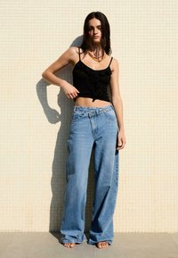 Széles szárú, világoskék farmernadrág, amelyet egy fekete, crop tank toppal párosítottak, fodros részletekkel. Természetes textúra, laza fit.