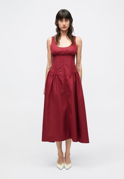Weinrotes, ärmelloses Kleid mit figurbetontem Oberteil und fließendem Rock. Hergestellt aus glattem Stoff, mit Falten und mittellangem Design.