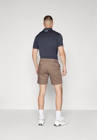 Mornarska polo majica s bijelim detaljima, u paru s smešnim kratkim hlačama. Outfit je upotpunjen bijelim čarapama i svijetlimtenama.