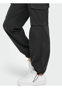 Losse zwarte cargobroek met zijzakken, een cuffed zoom met trekkoord, en gecombineerd met stevige witte sneakers.