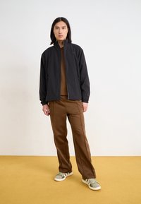 Černá lehká bunda, hnědý top a hnědé kalhoty. Tenisky mají zelené detaily. Jednoduchý design se zapínáním na zip a pohodlný střih.