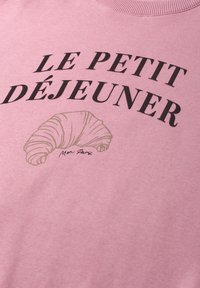 Tissu rose avec texte noir "LE PETIT DÉJEUNER" au-dessus d'un dessin au trait beige d'un croissant et d'un petit texte en cursive.