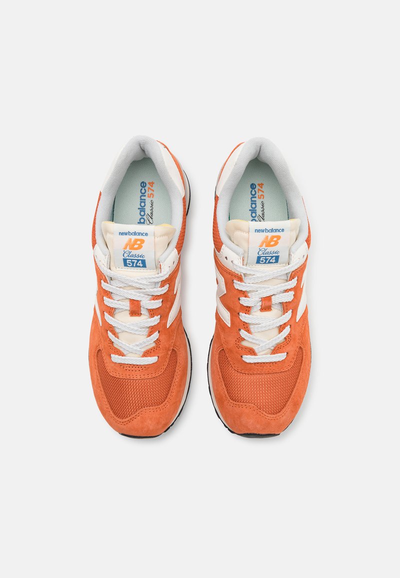 Baskets en daim orange et en mesh avec des accents blancs, dotées d'un col rembourré, d'un système de laçage et d'une semelle en caoutchouc. L'étiquette indique "New Balance 574."