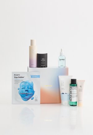 Forskellige hudplejeprodukter, inklusive en blå ansigtsmaske, toner, serumflasker, cremetuber og solcreme, arrangeret omkring en pastelfarvet gradientæske.