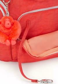 Zaino rosso in tessuto con una tasca con zip. Presenta un portachiavi a forma di scimmia rossa pelosa attaccato e un rivestimento interno liscio.