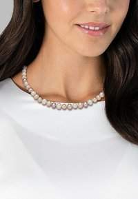 Pearl necklace featuring varying sizes of white and pink pearls, smooth texture, strung on a delicate gold wire, worn against a white garment.