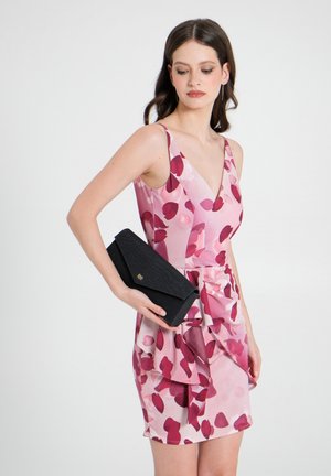 Rosa Blumenkleid mit V-Ausschnitt und rüschierter Taille. Schwarze, texturierte Clutch mit goldenen Akzenten, die in der rechten Hand gehalten wird.