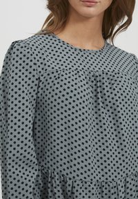 Abito grigio a pois con pois neri, scollatura rotonda, dettaglio arricciato in vita e maniche lunghe con vestibilità comoda.