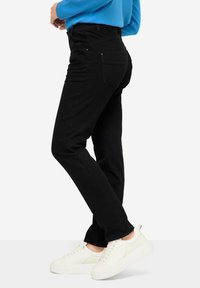 Vaqueros negros de corte slim y diseño de cinco bolsillos, con una cintura alta, un ligero estiramiento y combinados con zapatillas blancas.