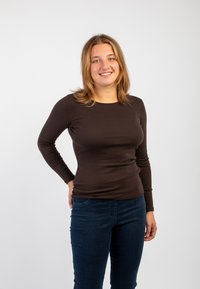 Camicia aderente a maniche lunghe marrone realizzata in materiale elasticizzato, abbinata a jeans blu scuro. Design semplice con scollatura rotonda. Sfondo bianco.
