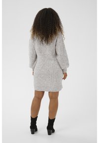 Szürke kötött pulóverruha texturált kábelmintával, ballon ujjal és bordás szegéllyel. Fekete magassarkú bokacsizmával viselve.