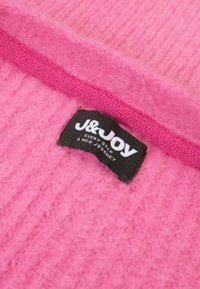 Fluffy roze stof met een geribbeld patroon; heeft een zwart label met "J&JOY" en witte tekst, tegen de levendige roze achtergrond.