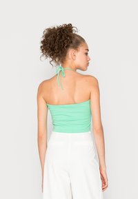 Top cropped halter verde menta com um design justo, apresentando laços finos no pescoço e uma textura de tecido lisa e elástica.