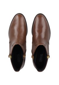 Botines de cuero marrón con una textura suave, puntera redondeada, cremalleras laterales y distintivos acentos de hardware dorado.