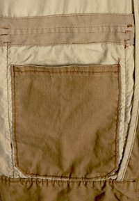 Tan färgad tygficka med beige kant; fyrkantig form med synlig sömnad; slät textur; minimalistisk design med en ren finish.