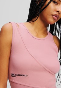 Roze geribbelde tanktop met uitsnijdingen op de schouders, voorzien van een borduring met logo aan de zijkant. Glad textuur, aansluitend ontwerp.