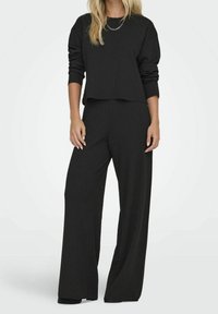 Schwarzes, geripptes Loungewear-Set mit einem cropped Langarmoberteil und weit geschnittenen Hosen aus einem weichen, strukturierten Stoff und lässiger Passform.