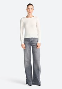 Top bianco a maniche lunghe con texture a coste, abbinato a jeans grigi a vita alta e gamba ampia con orlo grezzo.