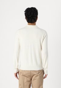 Pulôver de manga longa na cor creme, com colarinho, punhos e bainha canelados, feito de um material suave, usado sobre calças beige.