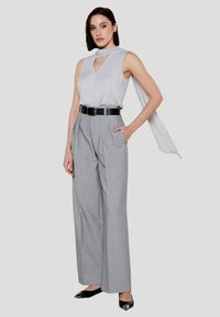 Top senza maniche grigio chiaro con scollatura profonda a V e dettaglio sciarpa, abbinato a pantaloni grigi a vita alta con pieghe e scarpe nere con punta affusolata.