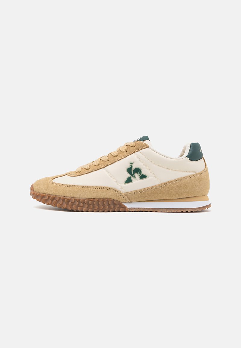 Zapatillas deportivas en beige y crema con un upper de ante texturizado, acentos verdes, una suela de goma con un dibujo en la banda de rodadura y un logo decorativo.