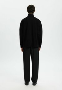 Chemise noire oversize avec un col haut, associée à un pantalon noir ample. Texture lisse, design minimal, vue de dos sur fond blanc.