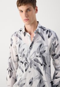 Hvit skjorte med knapper som har et svart og grått bladmønster, med en myk tekstur og klassisk kragedesign.