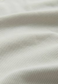 Svetlo béžová rebrovaná látka s jemnou textúrou. Povrch zobrazuje vodorovné pruhy, vytvárajúc jemný vzor.