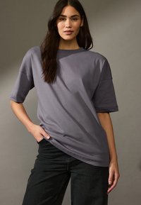 Violetinės per didelės marškinėliai su trumpomis rankovėmis, minkšta tekstūra, be siūlių dizainas ir laisvas kirpimas, derinami su tamsios denim kelnių.
