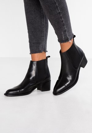 Sorte læderankelstøvler med lave blokhæle båret med mørkegrå skinny jeans med frynset kant.