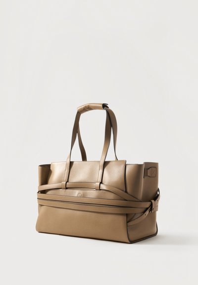 Grand sac fourre-tout en cuir beige avec double poignées et une sangle décorative enveloppante sur un fond blanc uni.