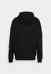 Sudadera con capucha negra que presenta una textura suave, puños acanalados y un diseño de texto multicolor en la manga izquierda.