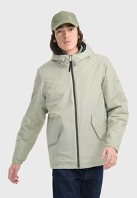 Hellgrüne wasserdichte Jacke mit Kapuze, Frontreißverschluss, zwei seitlichen Taschen und elastischen Bündchen. Kombiniert mit einer passenden Mütze.