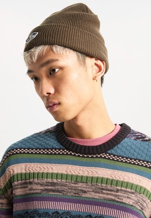 Brown ribbed beanie with logo patch, worn with a multicolored knit sweater featuring various textured patterns and a dark ribbed neckline.