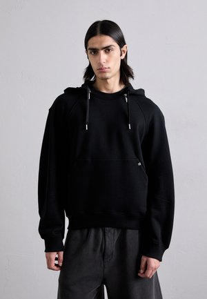 Czarna bluza z kapturem, wykonana z miękkiego materiału, z kieszenią kangurzą, regulowanymi sznurkami i luźnym krojem, z ribbowymi wykończeniami na rękawach i u dołu.