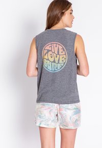 Šedé bezramínkové tričko s multicolorovým kulatým grafickým motivem a nápisem "Live Love Surf" na zádech, spárované se světlými pastelovými květinovými šortkami.