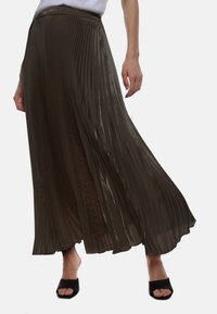 Gonna maxi plissettata di color marrone scuro, realizzata in tessuto leggero e lucido. Presenta una vita elastica e una consistenza morbida. Sandali neri open-toe.